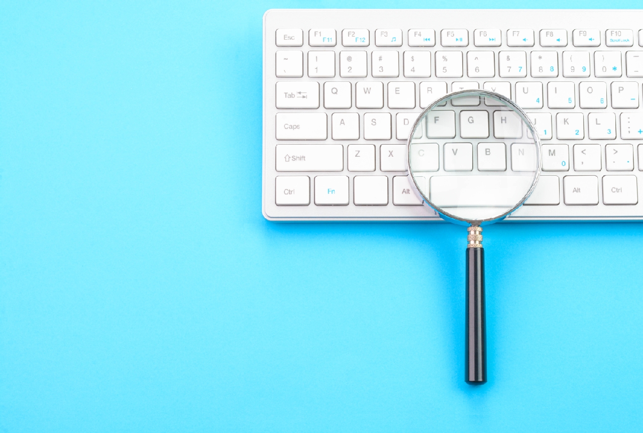 Magnifying glass on top of a white keyboard against a bright blue background, illustrating the concept of bringing something into focus.
