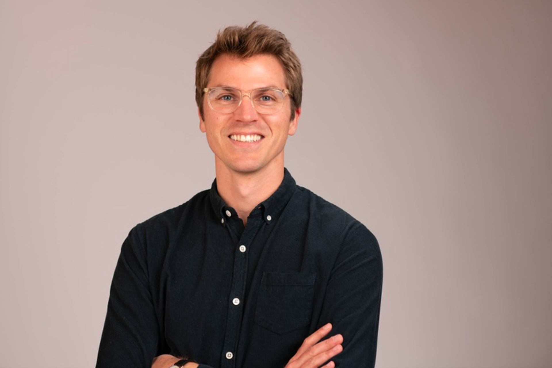 Photo of Andrew Ofstad, wearing glasses in a dark blue shirt against a gray background