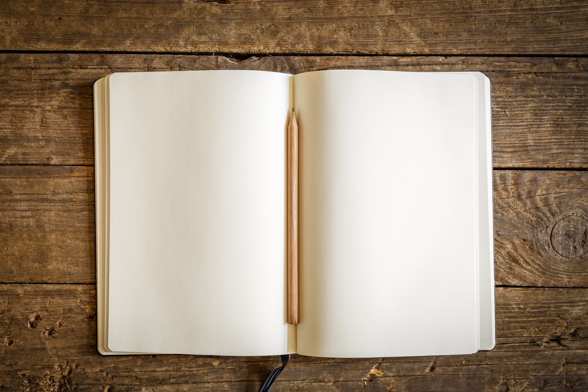 An empty notebook with a pencil down the crease on a wood table.