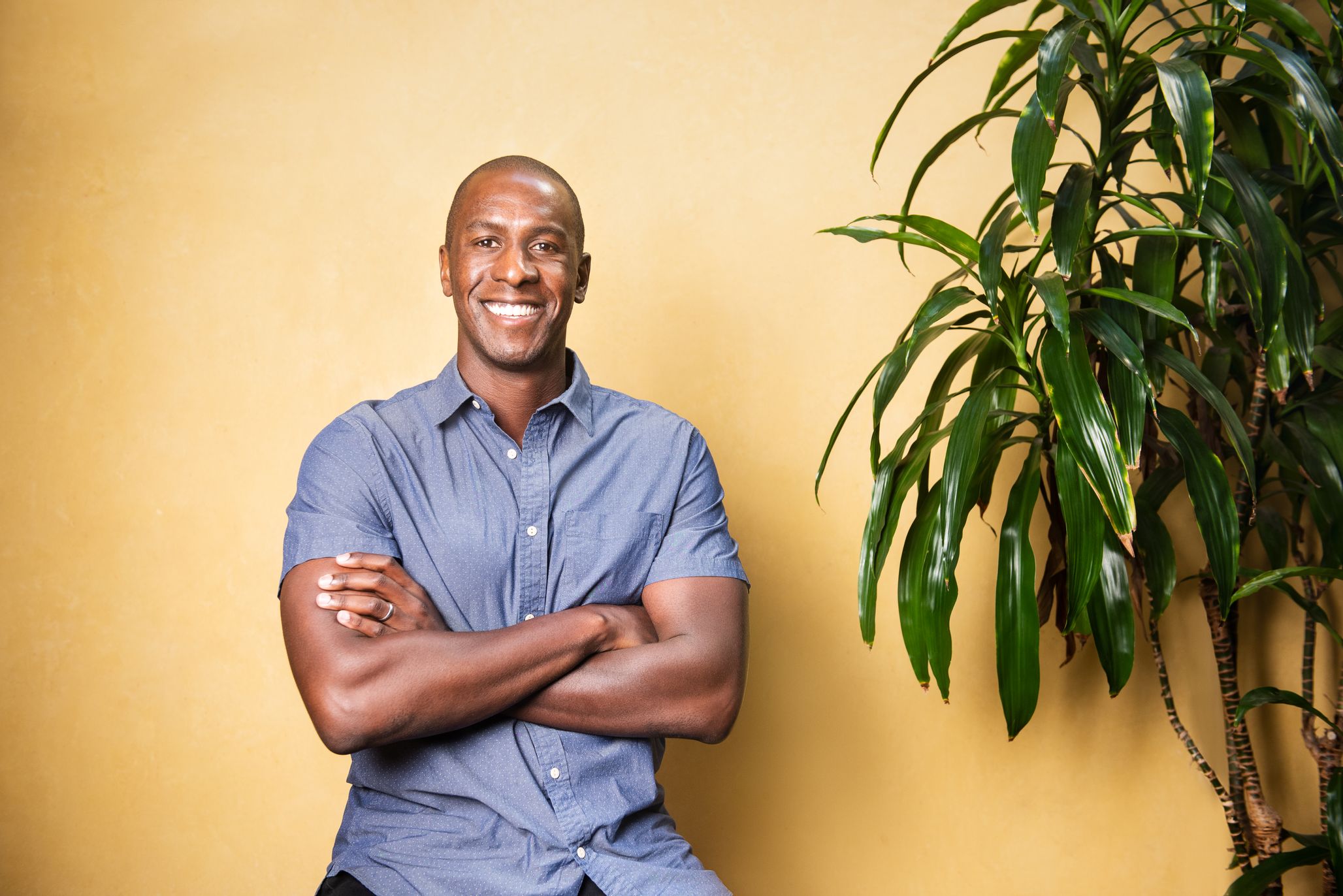 Photo of Meka Asonye seated with arms crossed against a yellow backdrop