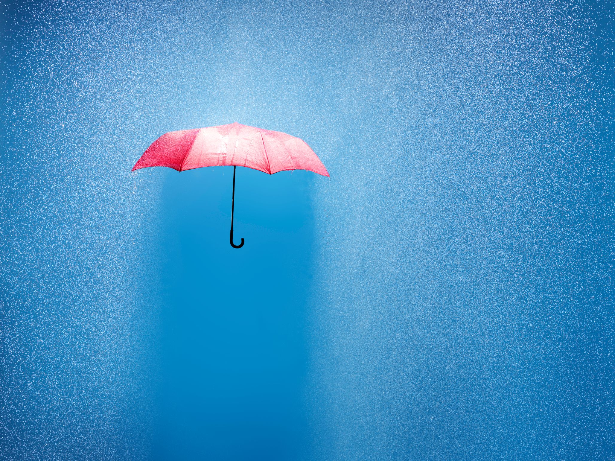 Photo of a red umbrella against a blue backdrop and a lot of rain.